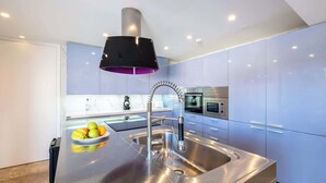 A modern kitchen with stainless steel appliances, a central island with a sink, and a black pendant light.
