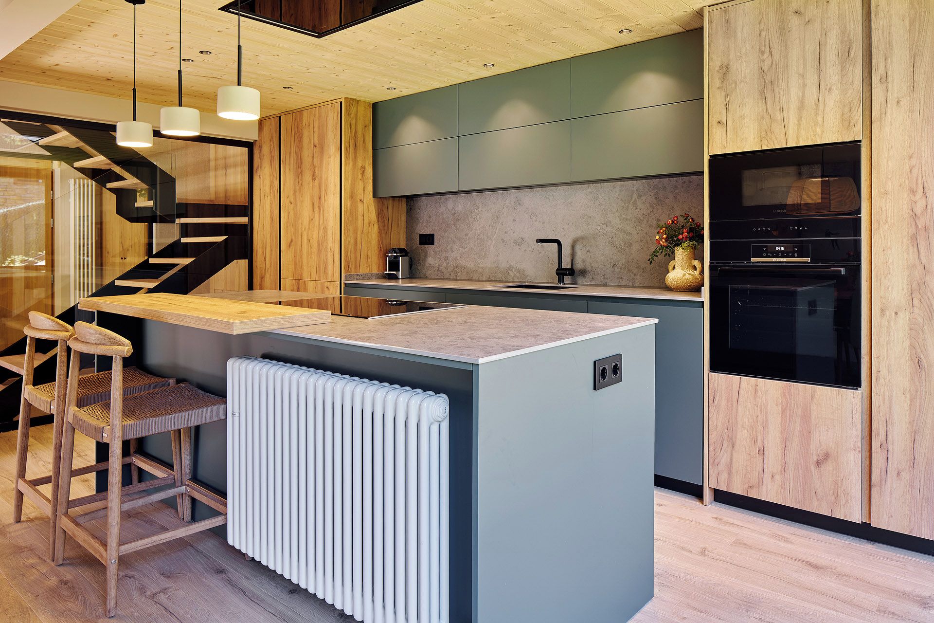 Une cuisine moderne dotée d’un îlot central, d’appareils électroménagers intégrés et d’un escalier en bois.