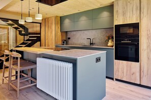 A modern kitchen with a central island, built-in appliances, and a wooden staircase. - Casa Garona by FeelFree Rentals (Vielha)