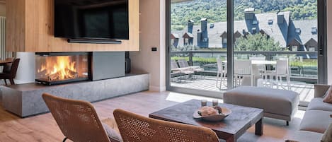 A modern living room with a fireplace, comfortable seating, and a large window overlooking a scenic landscape.
