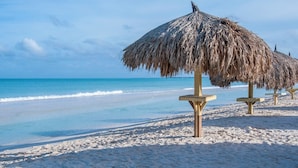 A beach with thatched umbrellas and wooden benches. - Yoyita Suites Aruba (Noord)