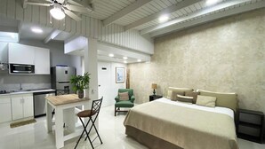 A modern hotel room with a large bed, a small desk, a chair, a dining area with a table and chairs, and a kitchenette. - Yoyita Suites Aruba (Noord)
