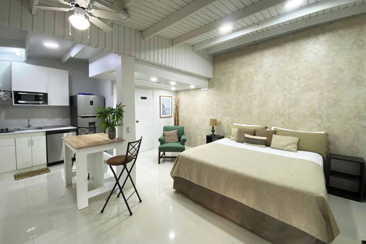 Een moderne hotelkamer met een groot bed, een klein bureau, een stoel, een zithoek met een tafel en stoelen, en een kitchenette.