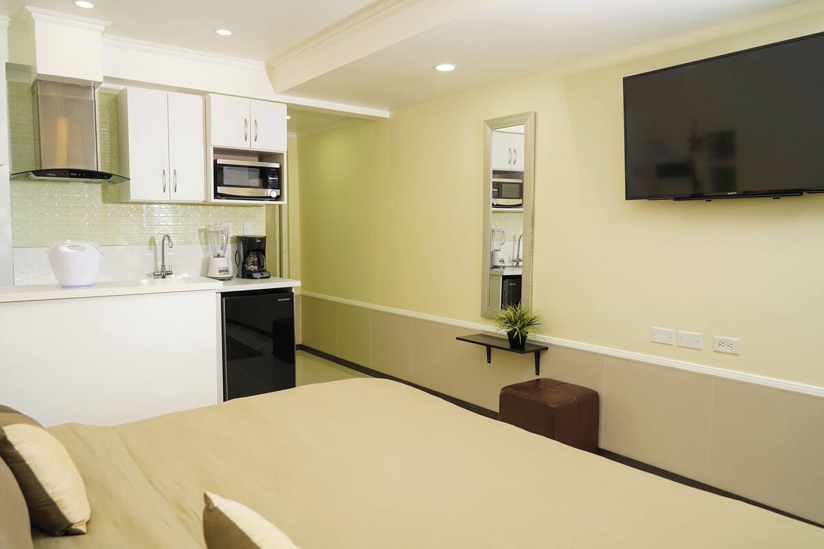 Een moderne hotelkamer met een kitchenette, een bed, een televisie en een zithoekje.