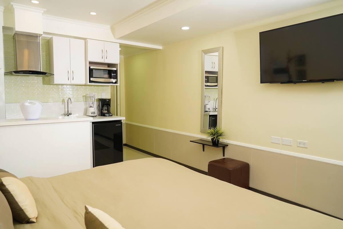 Een compacte hotelkamer met kitchenette, een bed, een televisie en een klein zithoekje.
