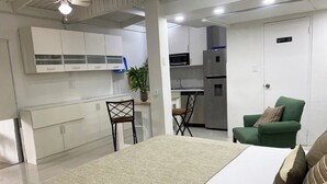 A modern hotel room with a bed, a green armchair, a dining area with a table and chairs, and a kitchenette. - Yoyita Suites Aruba (Noord)