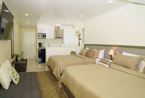 Habitación de hotel con dos camas, un kitchenette, un televisor de pantalla plana y un pequeño rincón de descanso.