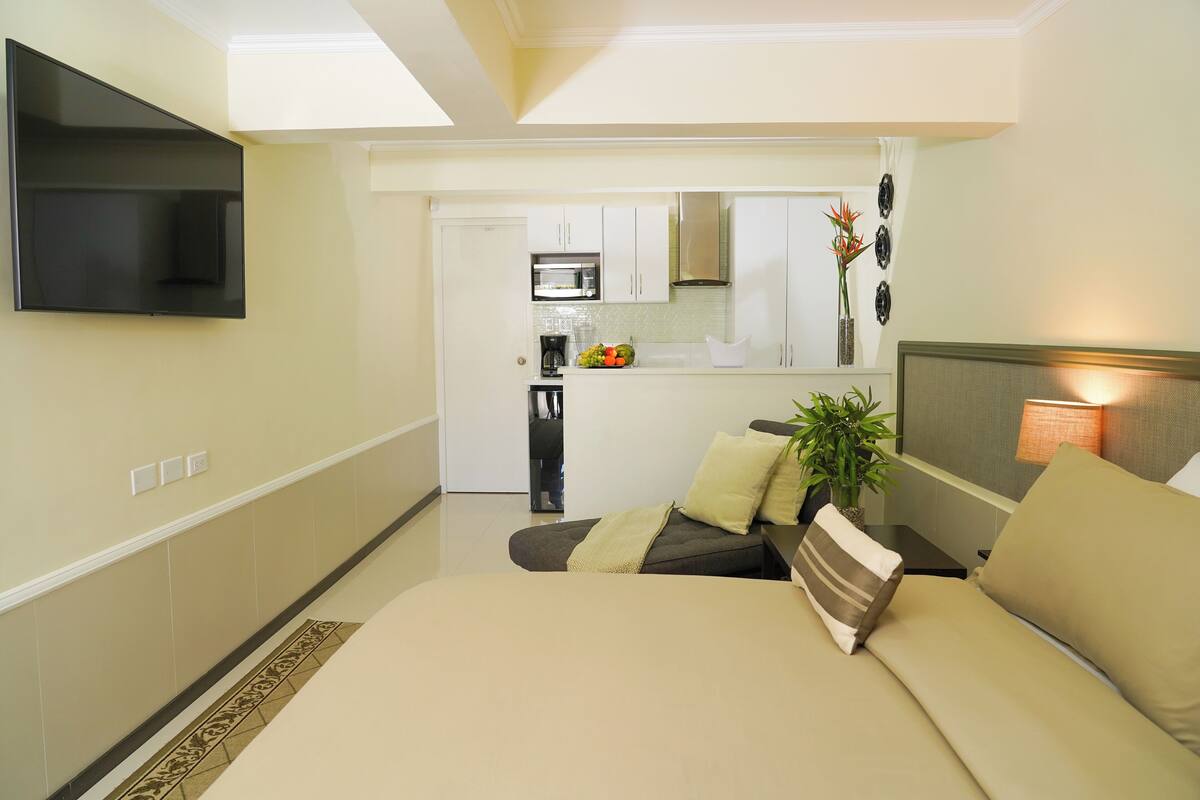 Een kleine hotelkamer met een bed, een aan de muur bevestigde televisie, een kitchenette en een badkamer die door een open deur zichtbaar is.