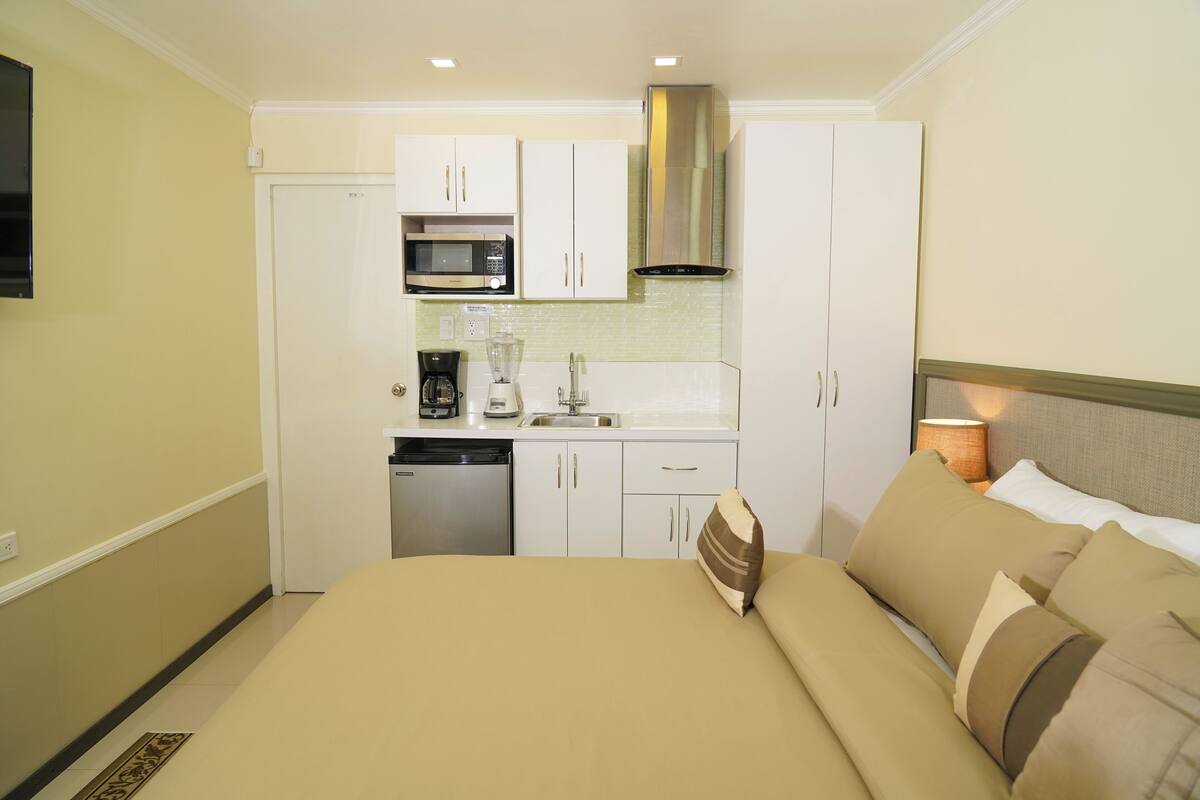 Een hotelkamer met een bed, kitchenette en een aan de muur bevestigde televisie.