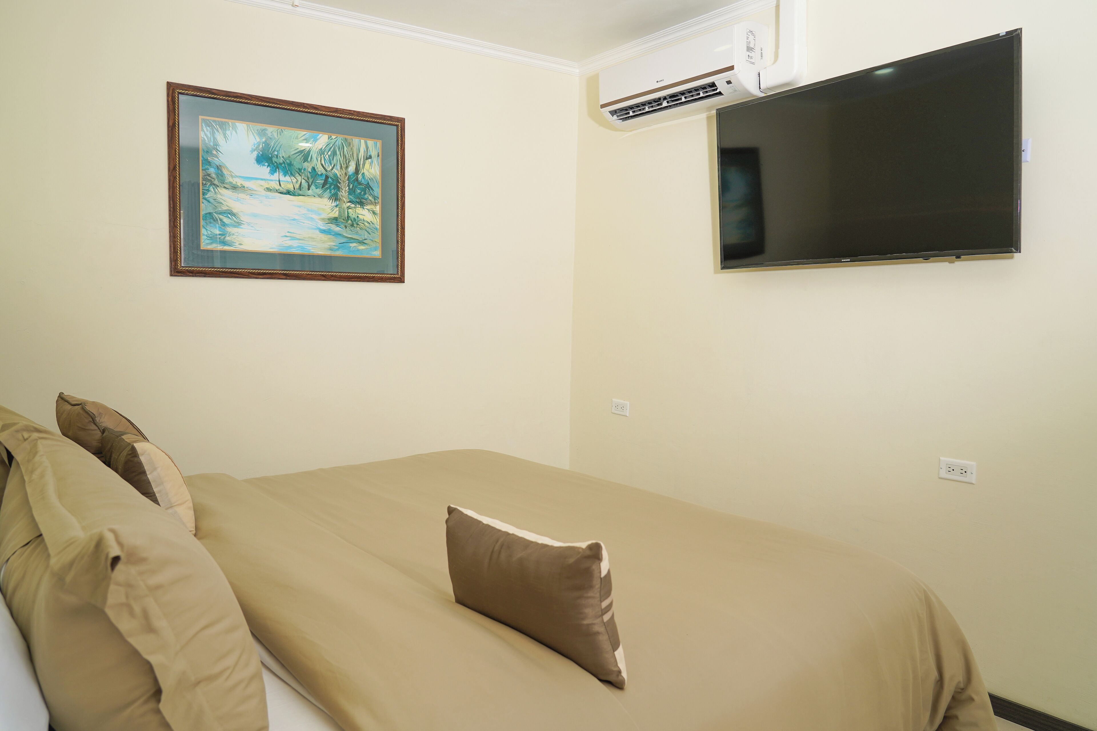 A hotel room with a bed, a painting on the wall, and a flat-screen TV mounted above it.