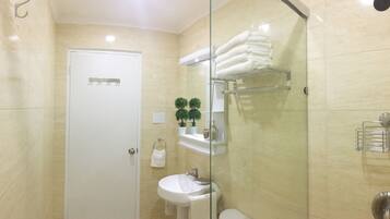 A bathroom with a white door, a sink, a glass shower enclosure, and shelves with towels and toiletries.