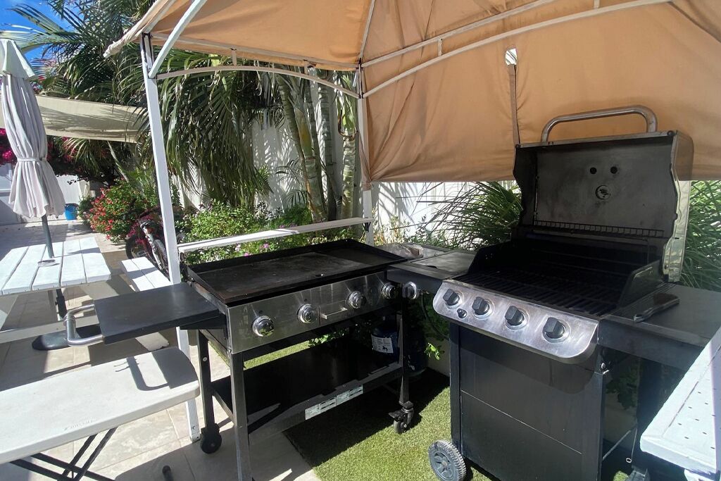 Una zona de barbacoa con una parrilla y una mesa plegable bajo una cubierta.