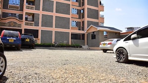 A multi-story building with a parking area in front. - Stay.Plus 1 bedroom Imperial Heights (Ruiru)