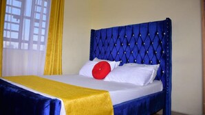 A bed with a blue upholstered headboard, white bedding, and a yellow throw blanket. - Stay.Plus 1 bedroom Imperial Heights (Ruiru)
