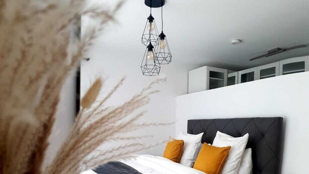A modern bedroom with a bed, a bedside table, and a hanging light fixture. - 2BD high end Apt. 134m2 in Strassen (Strassen)