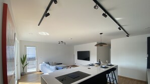 A modern kitchen with a central island, black bar stools, and a dining area with a long table and chairs. - 2BD high end Apt. 134m2 in Strassen (Strassen)