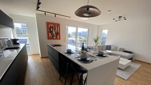 A modern kitchen with a central island, a dining area with a white table set, and a living room with a grey sofa. - 2BD high end Apt. 134m2 in Strassen (Strassen)
