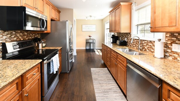 A kitchen with wooden cabinets, granite countertops, stainless steel appliances, and a tiled backsplash. - 3BR Walk to the Beach House in Surfside Beach! Looney Dunes (Surfside Beach)