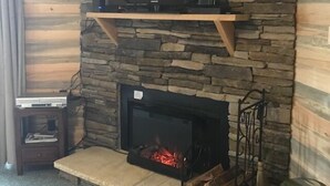 A living room with a stone wall, a mounted television, a fireplace with logs, and a small table. - 2208  Hot tub, sauna & more resort amenities - Paradise in the Mountains (Beech Mountain)