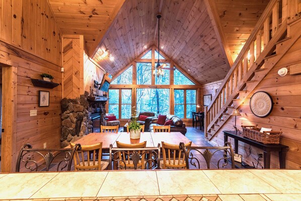 Cozy cabin interior with a high ceiling, stone fireplace, and wooden dining table.