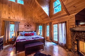 Cozy bedroom with a large bed, stone fireplace, and wooden bench.