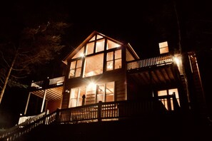 Guests can enjoy a spacious balcony with a railing, surrounded by trees, from the upper level of this cabin.