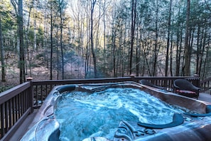 Relax on the deck with a hot tub surrounded by a serene forest setting.