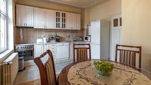 A compact kitchen with white cabinets, a stove, a microwave, and a refrigerator. There is a dining table with chairs and a bowl of grapes. - Apartments Dobrinjska (Београд)