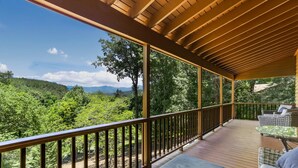 Eine überdachte Terrasse mit Blick auf eine bewaldete Landschaft und Berge.