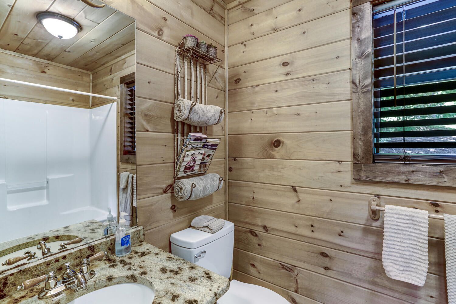 Ein Badezimmer einer Holzhütte mit Waschbecken, Toilette und einem Fenster mit Jalousien.