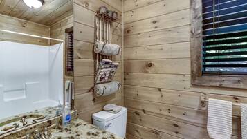 Ein Badezimmer einer Holzhütte mit Waschbecken, Toilette und einem Fenster mit Jalousien.