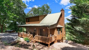 Eine Holzhütte mit Veranda und Schornstein, umgeben von Bäumen.
