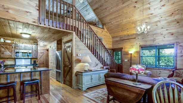 Ein rustikales Blockhaus-Interieur mit einer Holztreppe, einer Küche mit Barbereich und einer gemütlichen Sitzecke mit Lampe.
