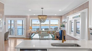 A spacious kitchen with a large island, a dining area with a view of the sea, and a chandelier. - The Hydeaway | Pet Friendly, Soundfront with Dock! (Topsail Beach)
