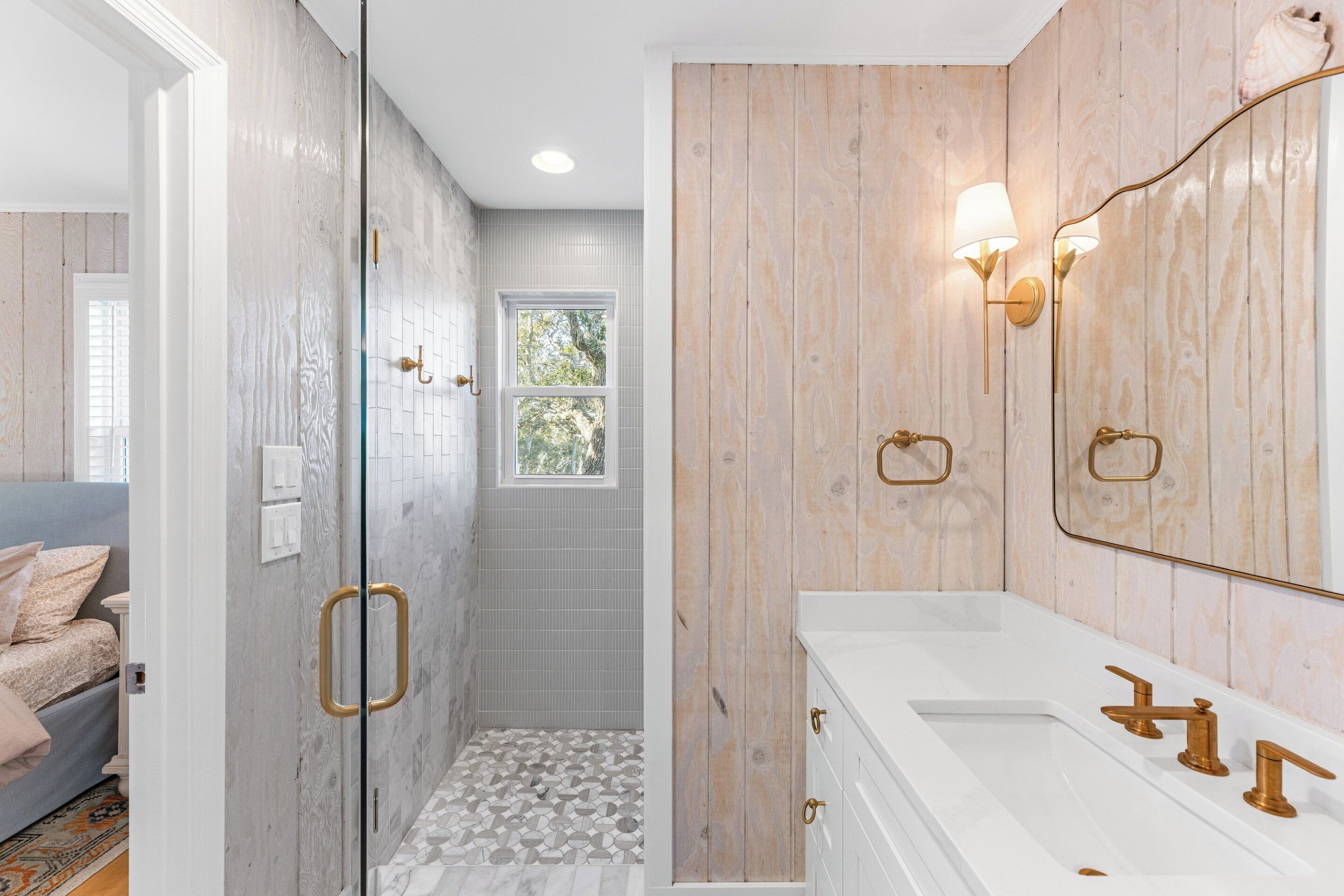 Ein Badezimmer mit Dusche, Waschbecken mit goldfarbenen Armaturen und einer Holzwandverkleidung.
