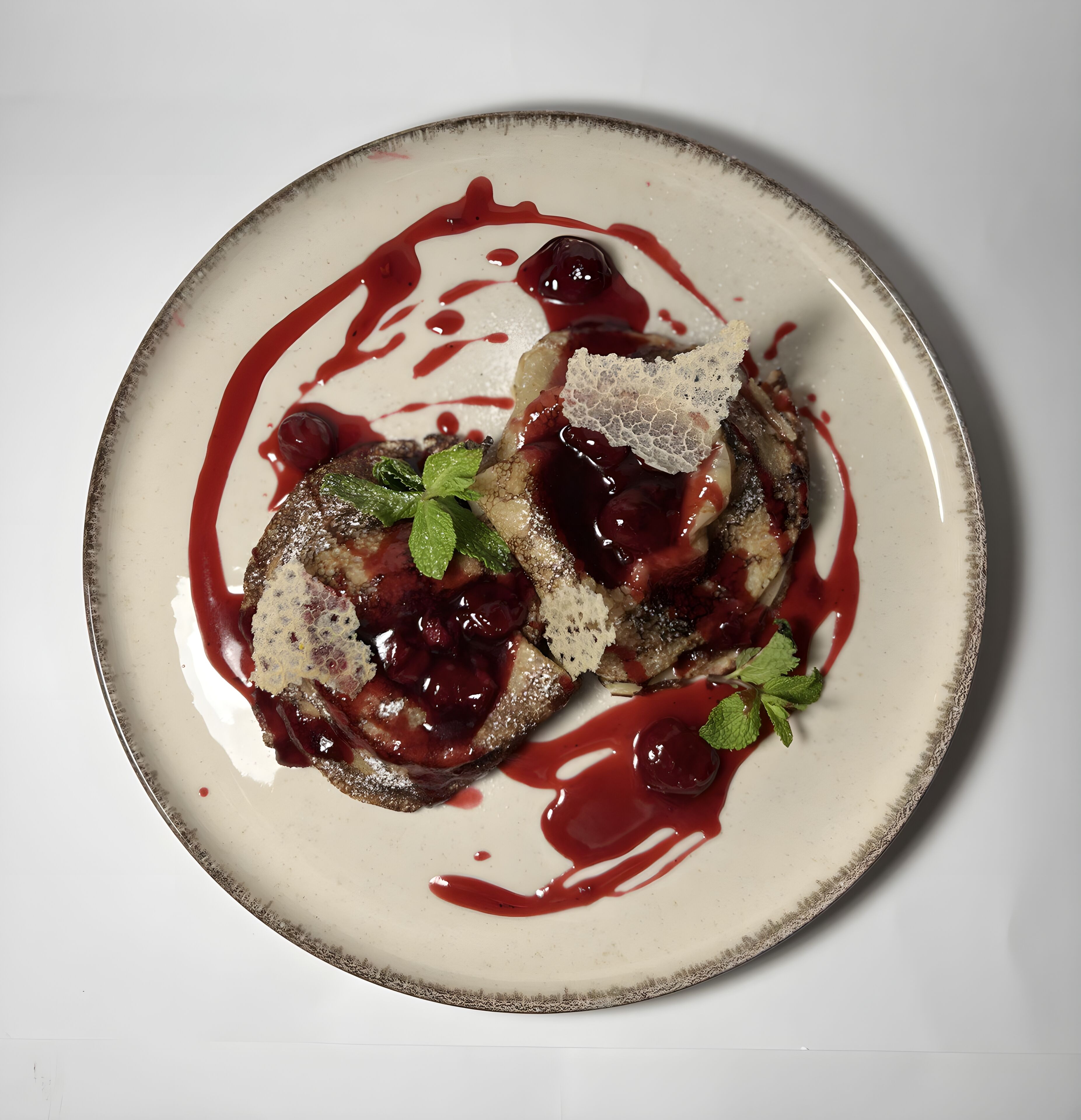 Un plato de postre con una porción de pastel, compota de frutos rojos y adorno de menta.