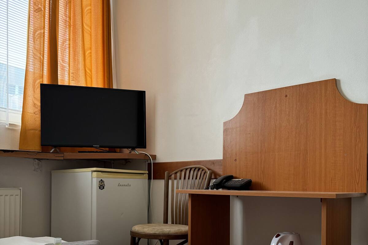 A hotel room with two beds, a television, a minibar, a chair, a desk with a telephone, and a kettle.