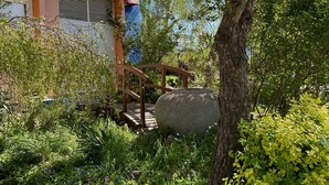 Un jardín con un puente de madera, una maceta de piedra grande y un edificio de fachada azul y naranja.