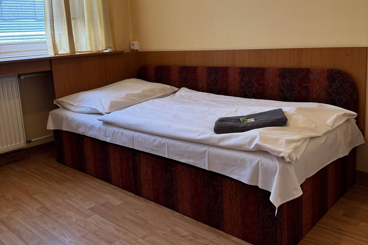 A single bed with a wooden headboard, white bedding, and a folded towel.