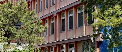A multi-story building with a pink facade, large windows, and a balcony on the second floor.