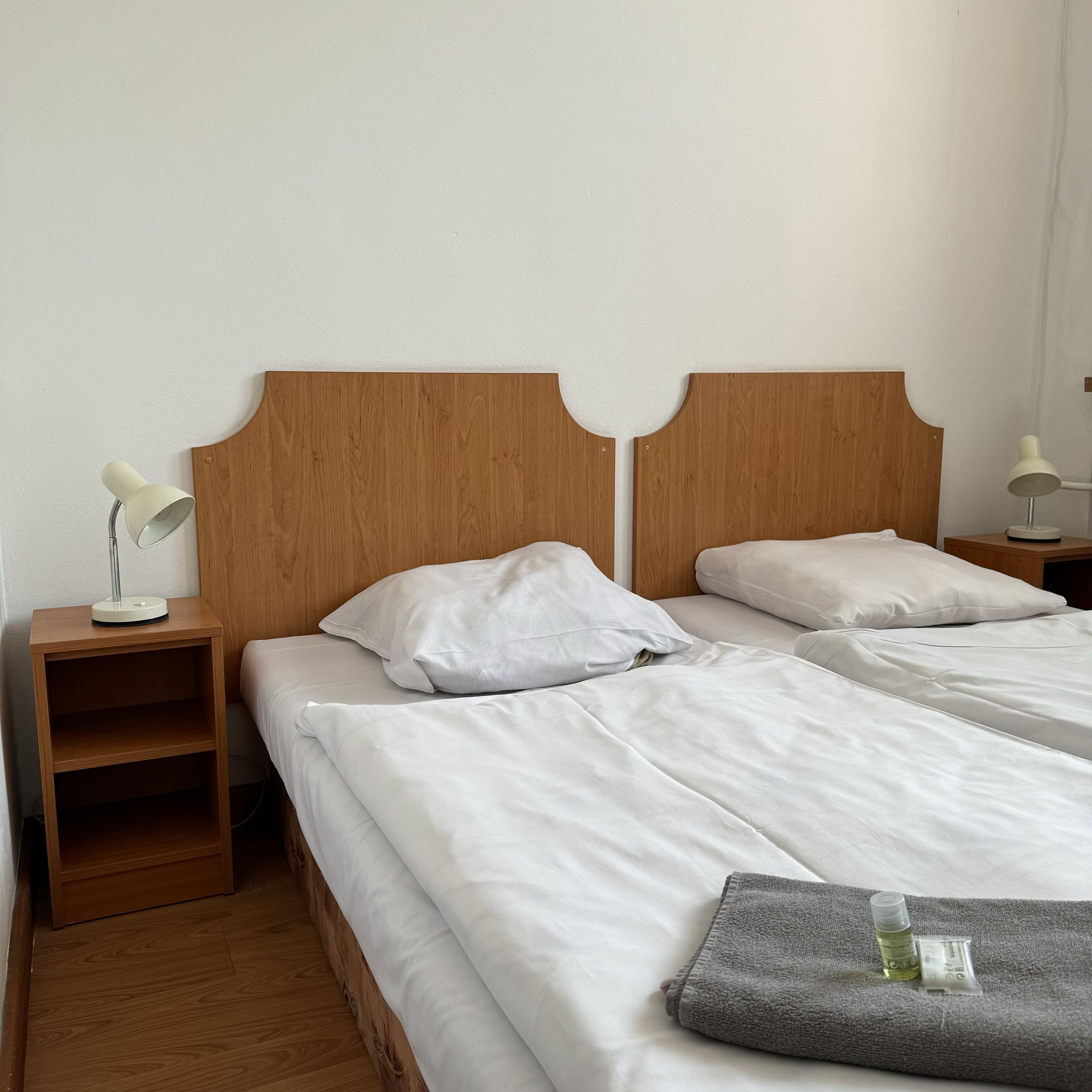 Un lit double avec du linge de lit blanc, une tête de lit en bois et une table de chevet avec une lampe.