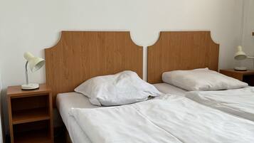 Un lit double avec du linge de lit blanc, une tête de lit en bois et une table de chevet avec une lampe.