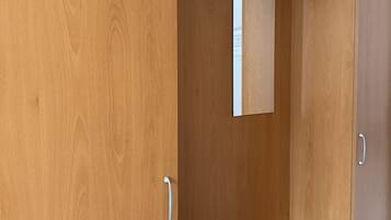 A wooden wardrobe with a single door open, revealing a mirror and a hanging hook.