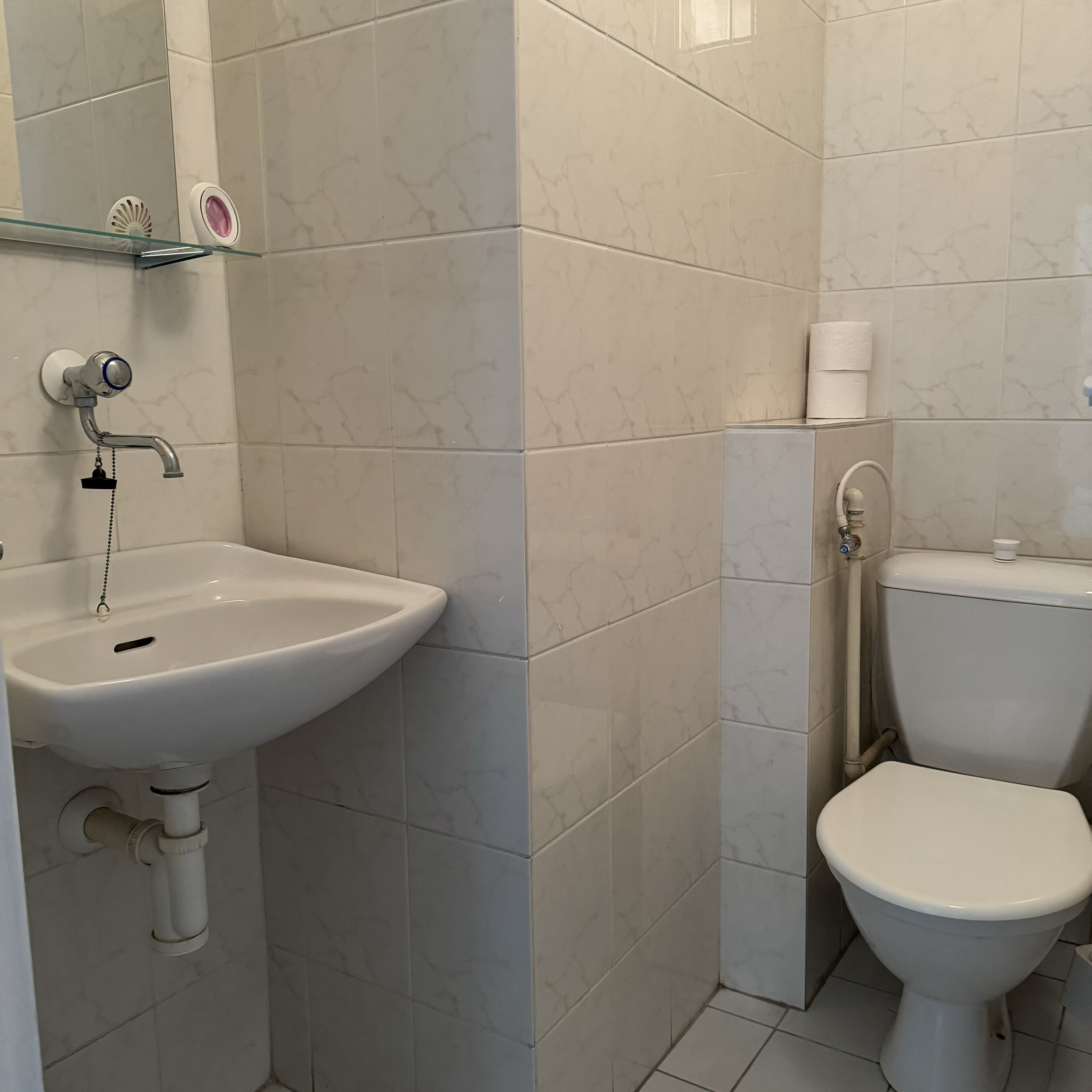 Un baño con un lavamanos blanco, un inodoro y una repisa de vidrio con artículos de aseo.