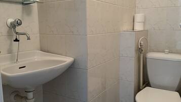 Un baño con un lavamanos blanco, un inodoro y una repisa de vidrio con artículos de aseo.