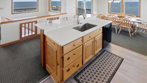 Een moderne keuken met een groot eiland, houten kasten en uitzicht op zee door grote ramen.