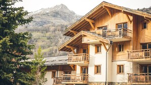 A multi-story wooden building with balconies, set against a mountainous backdrop. - Le Serre d'Or, large apartment at the foot of the slopes (Saint-Chaffrey)