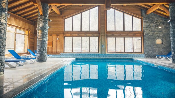 An indoor swimming pool with wooden beams and stone walls, surrounded by blue lounge chairs. - Le Serre d'Or, large apartment at the foot of the slopes (Saint-Chaffrey)