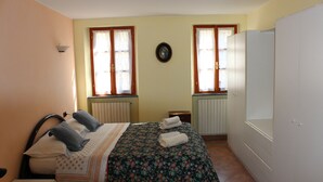 A bedroom with a bed, two windows, a radiator, a wardrobe, and a wall clock.