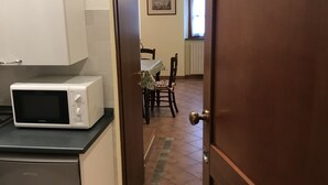A kitchen with a microwave and a refrigerator, leading to a dining area with a table and chairs.